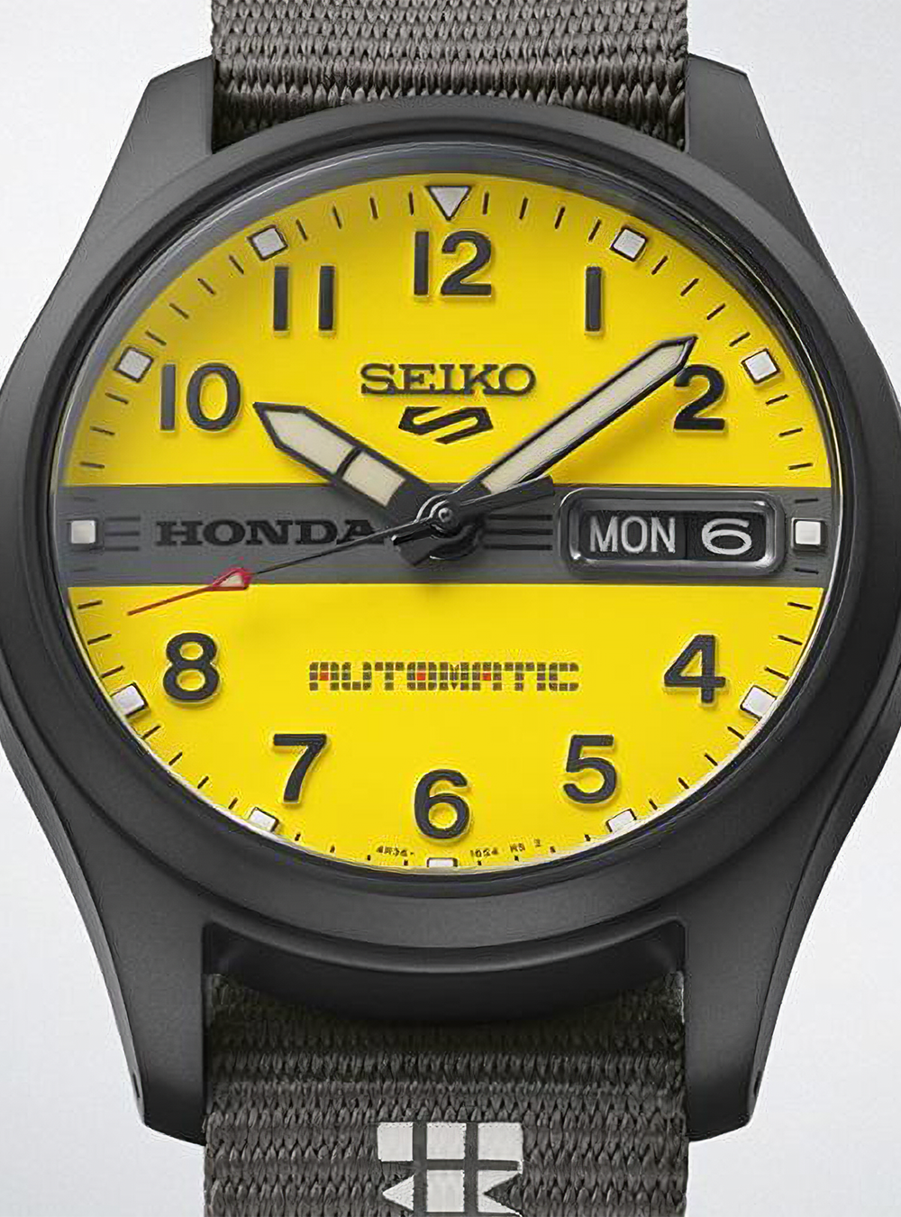 Seiko Honda Automatic watch with a bright yellow dial, black case, and textured gray fabric strap.