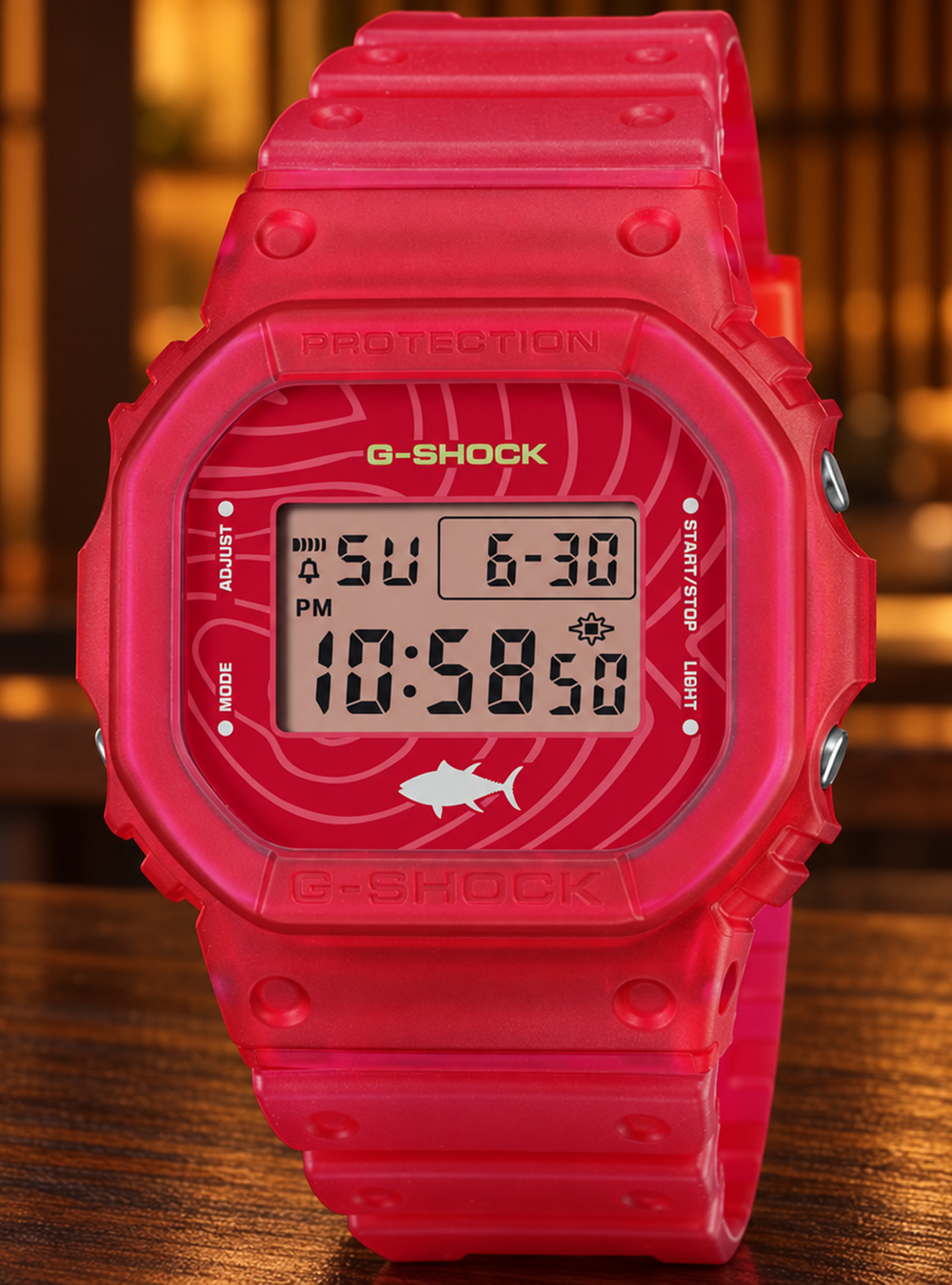 A bright pink G-Shock digital watch with a matching pink strap, resting on a dark wooden surface with a warm, blurred background.