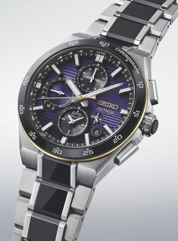 A Seiko Astron wristwatch with a silver titanium  link bracelet, black inlay segments, and a dark purple sunburst dial with black subdials and a gold-tone bezel.