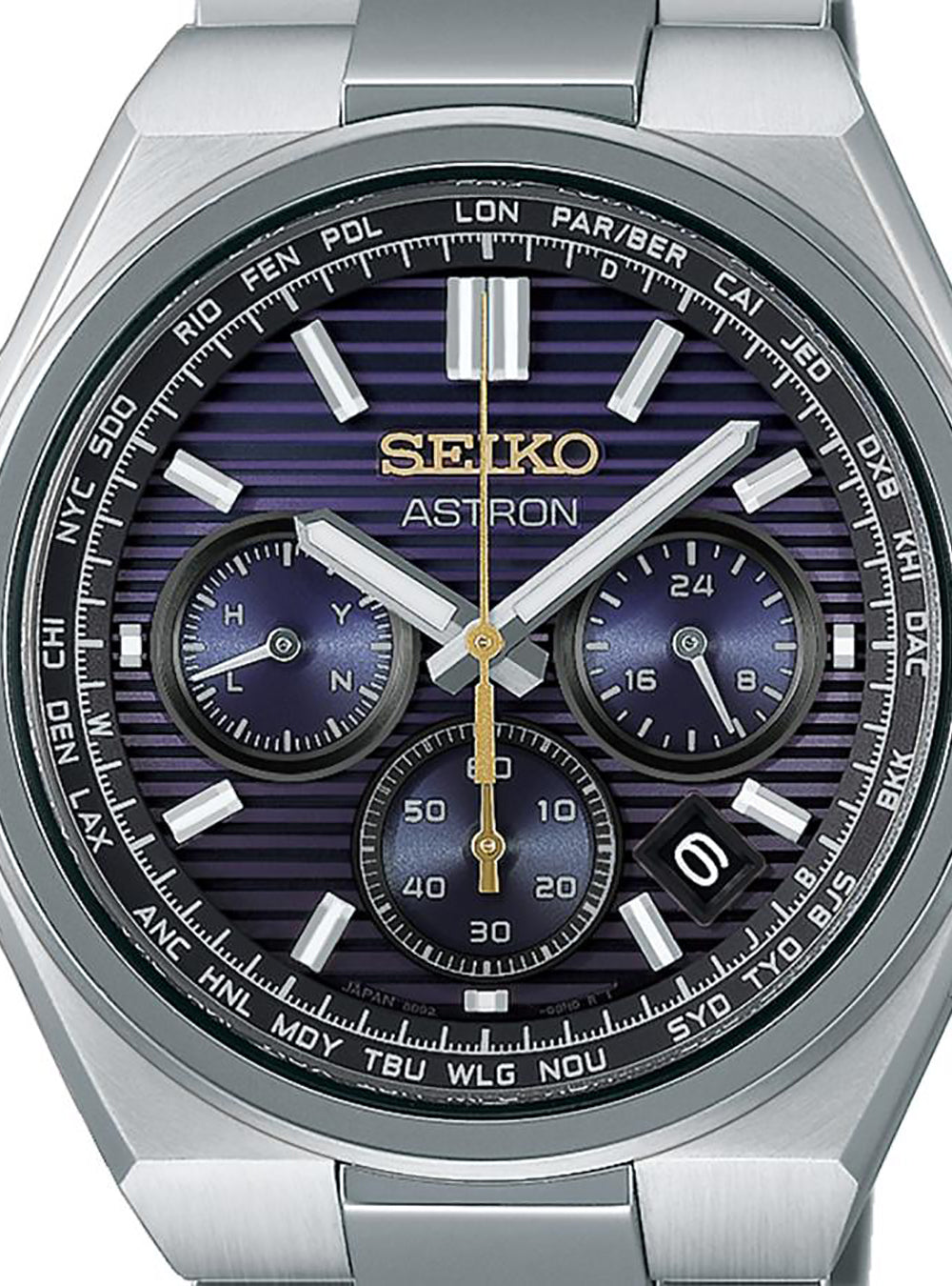 A close-up of a Seiko Astron wristwatch with a brushed silver-tone metal case and bracelet, featuring a dark blue and purple striped dial with white, silver, and gold details.