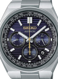 A close-up of a Seiko Astron wristwatch with a brushed silver-tone metal case and bracelet, featuring a dark blue and purple striped dial with white, silver, and gold details.