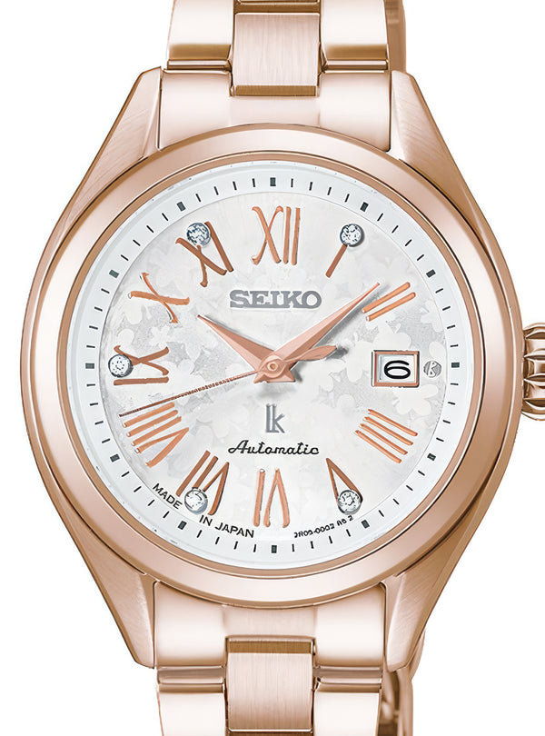 A Seiko women's automatic watch featuring a rose gold-tone metal bracelet and case, a white dial with rose gold Roman numerals and hands, and crystal hour markers.