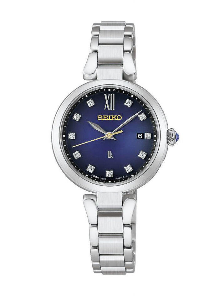 A Seiko women's watch featuring a polished silver titanium link bracelet, a round silver case, and a deep blue dial with gold-tone hands and Roman numeral XII.